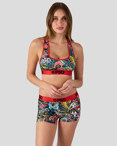 Woman wearing colorful floral and bird print sports bra and shorts set with red trim and PSD branding.