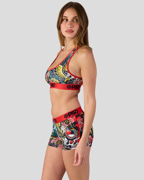 Woman wearing colorful winged graphic sports bra and matching shorts with red waistband and multicolored tattoo-style print.