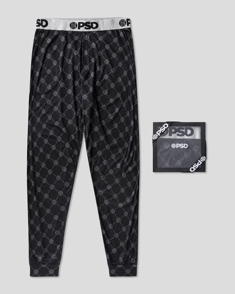 Black lounge pants with repeated monogram print and PSD branded waistband, shown with product packaging.