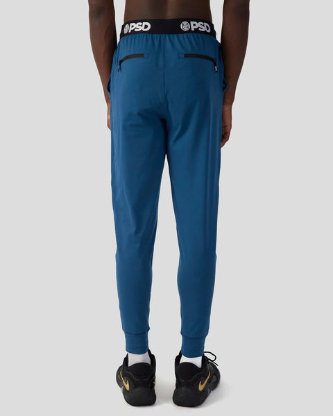 Deep teal joggers with black zip pockets, PSD waistband, and tapered ankles, shown from back view.