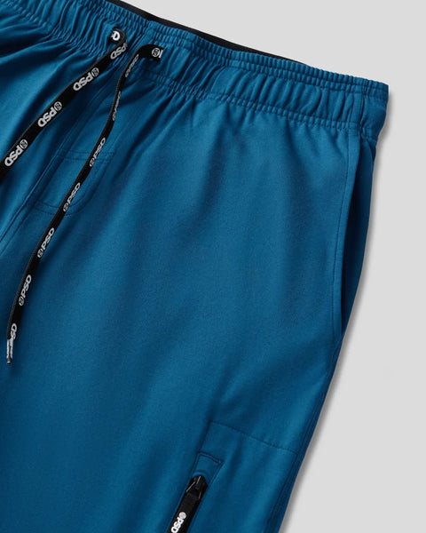 Deep teal jogger with elastic waistband, drawstring with branded stops, and ankle zipper detail.