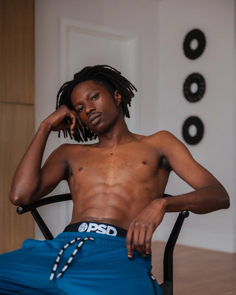 Man wearing deep teal joggers with drawstring waistband and branded elastic band, sitting in chair.