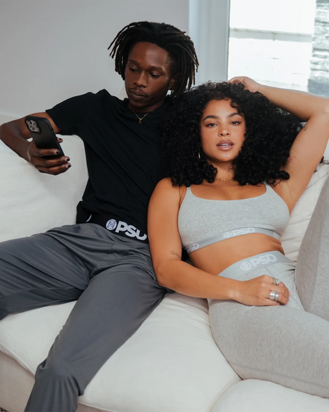 Charcoal lounge pant with elastic waistband and branded logo detail, shown on model seated on couch.