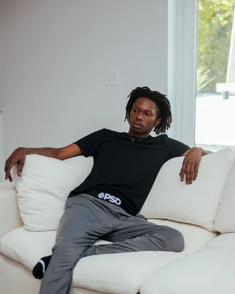 Charcoal lounge pants with elastic waistband worn by a man seated on a white sofa.