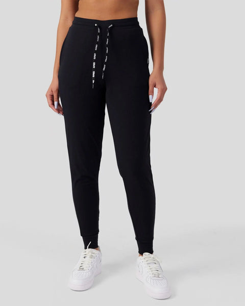 Black joggers with drawstring waist and tapered ankles, shown on model wearing white sneakers.