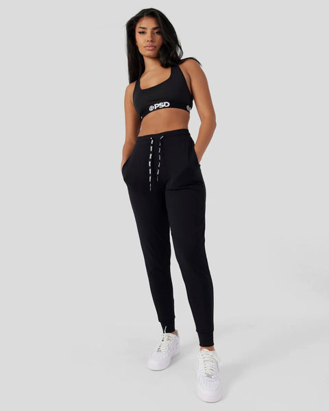 Black joggers with drawstring waist and tapered legs, shown with matching black crop top and white sneakers.