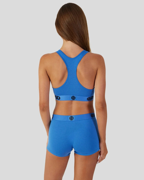 Woman wearing blue racerback sports bra and matching shorts with logo waistband.