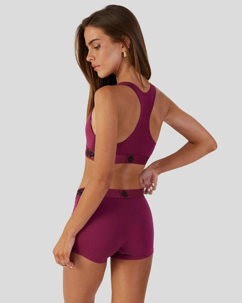Woman wearing a burgundy sports bra and matching shorts with open back design, shown from side view.