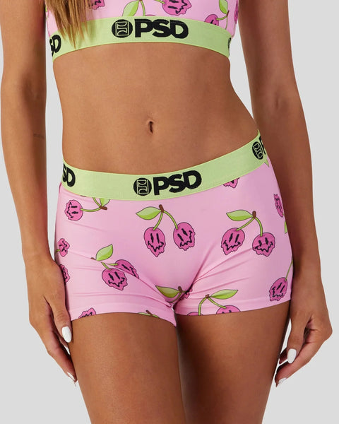 Person wearing PSD brand sports bra and boyshort underwear with pink fabric featuring purple fruit and green leaf print.