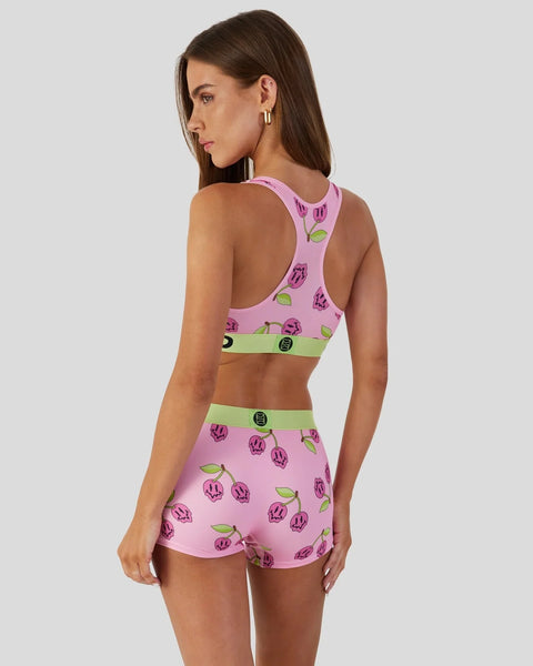 Woman wearing pink sports bra and shorts set with purple tulip print and lime green waistbands.