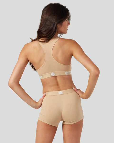 Woman wearing sand-colored modal sports bra and matching shorts with logo waistband, shown from back view.