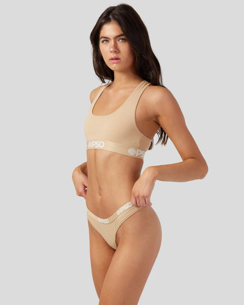 Woman wearing sand-colored racerback sports bra and matching briefs with logo waistband.