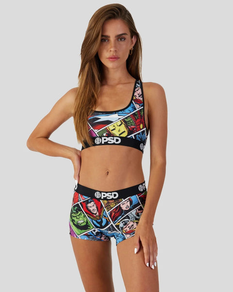 Woman wearing a Marvel Comics-print sports bra and shorts set with PSD branding and colorful superhero character graphics.