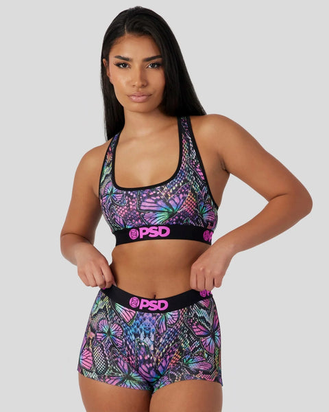 Purple butterfly-patterned sports bra and shorts set with black PSD waistbands worn by model.