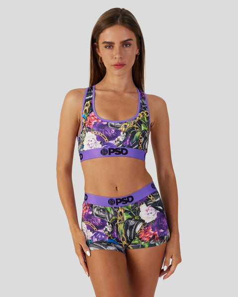 Woman wearing purple sports bra and matching shorts with colorful floral and gold chain print.