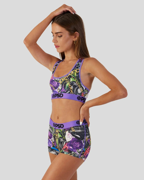 Woman wearing purple sports bra and matching shorts with colorful floral print and branded waistband.