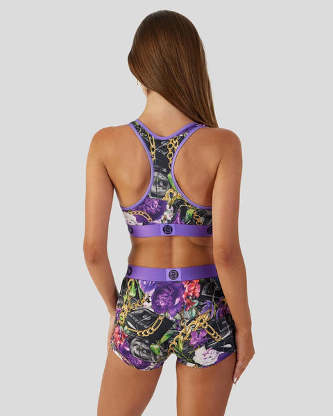Woman wearing purple sports bra and matching shorts with floral and chain print design, shown from back view.