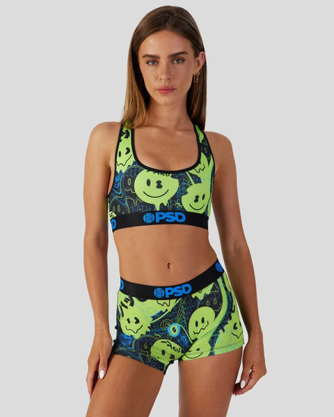 Woman wearing neon yellow and blue sports bra and shorts set with smiley face and cosmic print design.