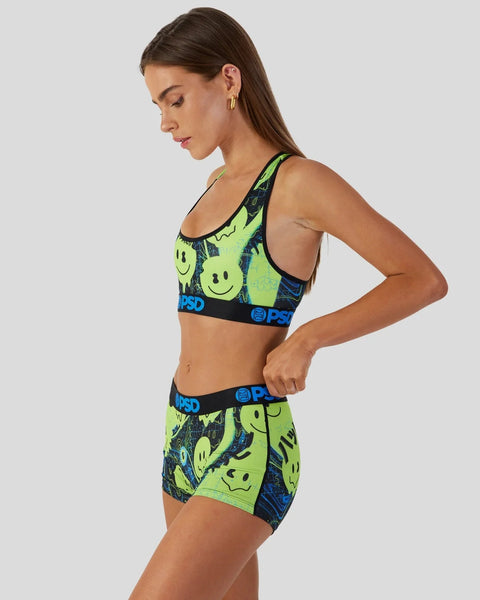 Woman wearing neon yellow and navy sports bra and shorts set with smiley face print and black waistband.