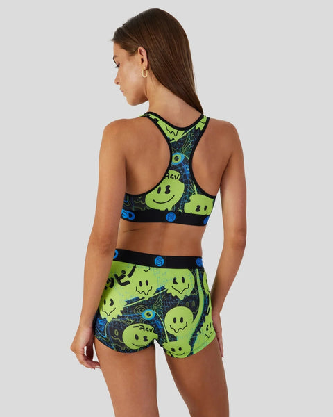 Woman wearing neon green and navy sports bra and shorts set with smiley face and cosmic print design.