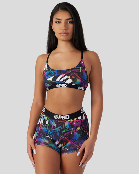 Woman wearing colorful Looney Tunes-themed sports bra and shorts set with neon cartoon graphics and PSD branding.