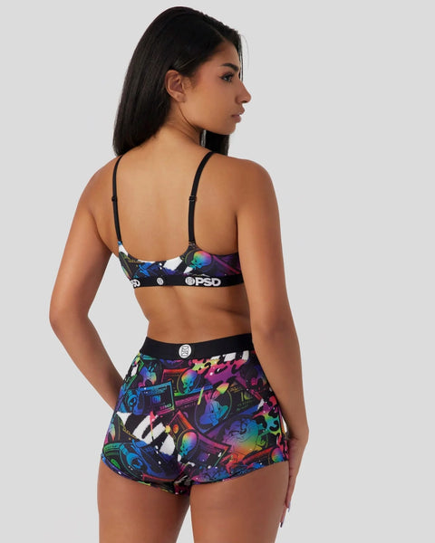 Woman wearing black bra and colorful patterned shorts with Looney Tunes and PSD branding, shown from back.