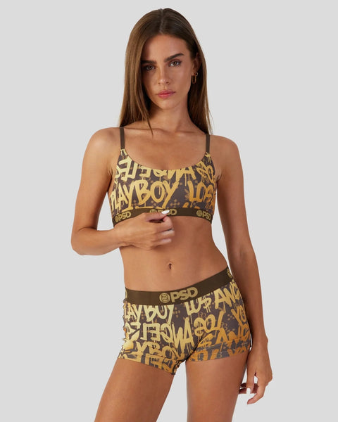 Woman wearing brown and gold graffiti-print sports bra and matching shorts set with Playboy branding.
