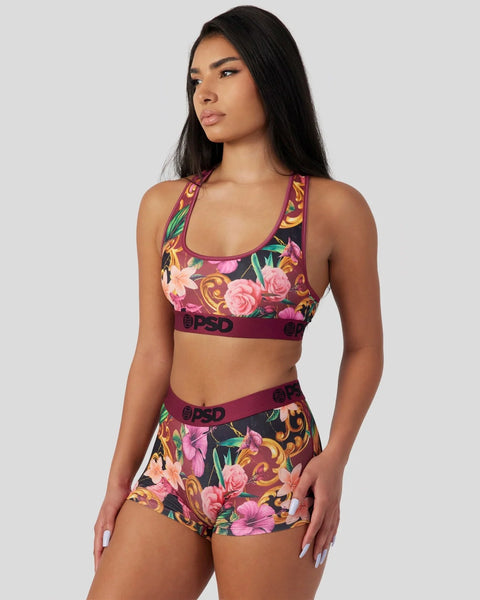 Woman wearing purple sports bra and shorts with pink floral and gold baroque pattern, branded waistband.