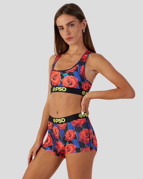 Woman wearing a racer-back sports bra and shorts with red roses on navy and blue background, black PSD waistbands.