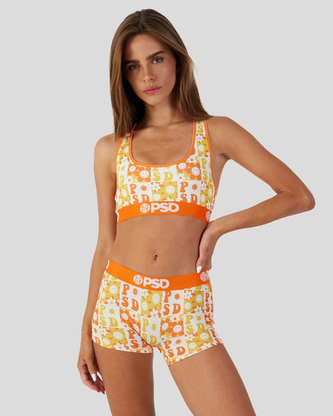 Woman wearing white, yellow, and orange checkerboard patterned sports bra and shorts set with orange elastic bands.