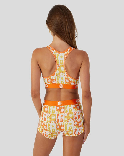 Woman wearing orange and yellow PSD checkers sports bra and matching shorts with floral pattern and logo details.