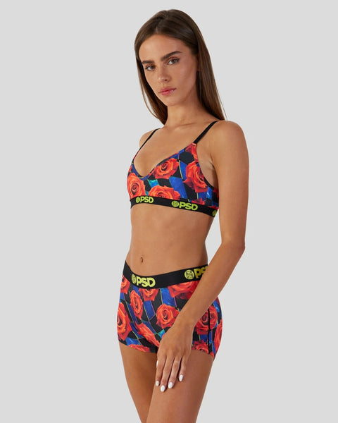 Woman wearing colorful floral racer bra and shorts set with red roses, blue background, and black elastic waistbands.