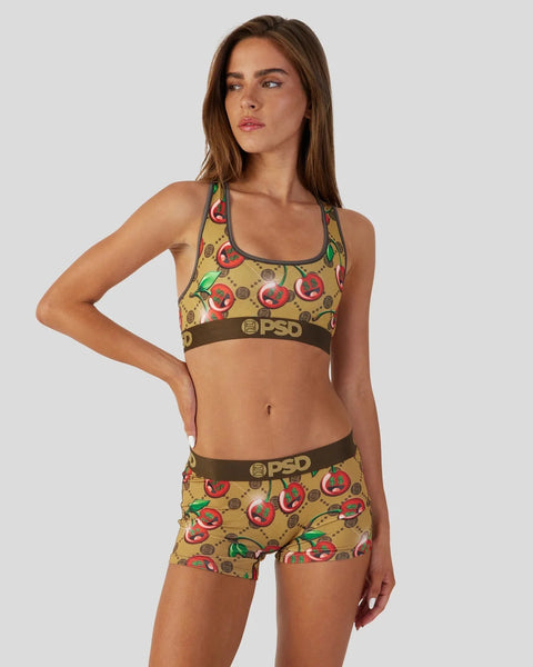 Woman wearing tan sports bra and shorts with red cherry and green leaf pattern and brown PSD waistbands.