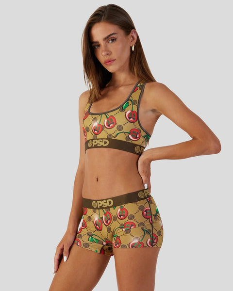 Woman wearing tan sports bra and shorts with cherry print and brown PSD waistband.