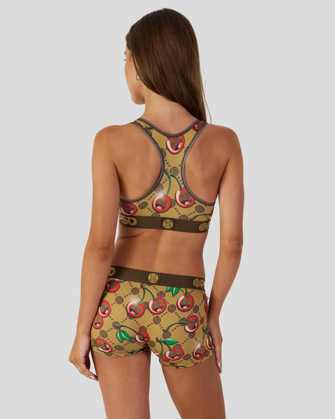 Woman wearing a yellow sports bra and shorts set with red cherry print and brown trim.
