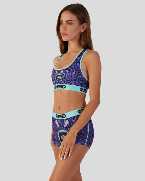 Woman wearing purple leopard print sports bra and shorts with turquoise trim and PSD branding.