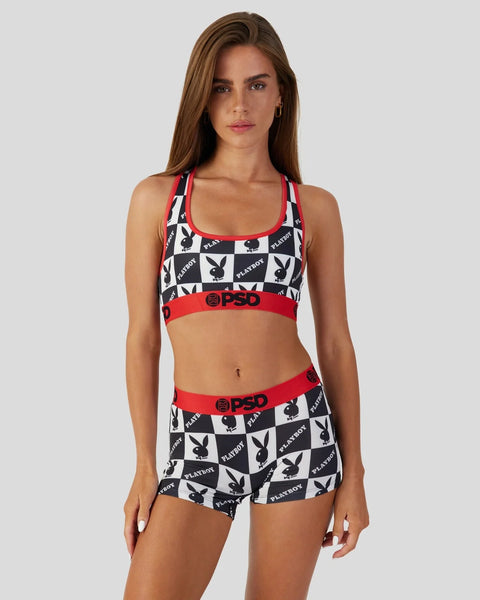 Woman wearing black and white checkerboard sports bra with red trim and matching shorts featuring Playboy logo pattern.