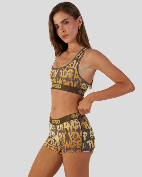 Woman wearing charcoal sports bra and shorts with gold graffiti print and branded waistband.