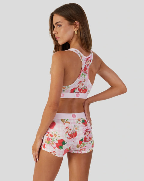 Woman wearing pink strawberry print sports bra and matching shorts set with white trim bands.