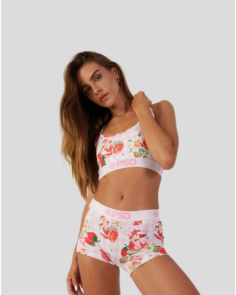 Woman wearing white sports bra and shorts with red strawberry and cake print pattern.