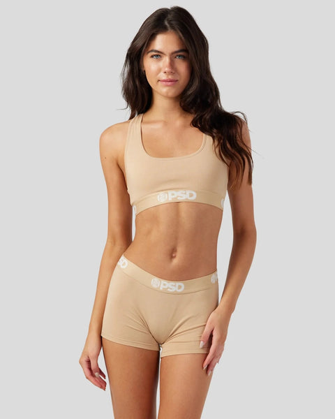 Woman wearing sand-colored racerback bra and shorts with branded waistband.