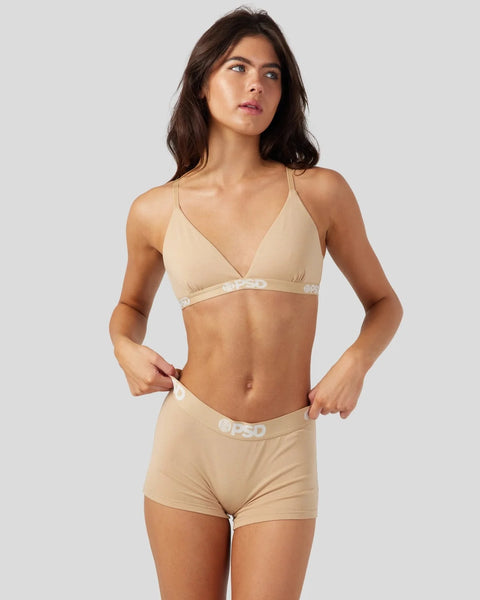 Woman wearing sand-colored bra and shorts set with adjustable straps and elastic waistband.