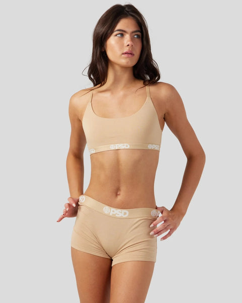 Woman wearing sand-colored modal sports bra and matching boy shorts with branded waistband.