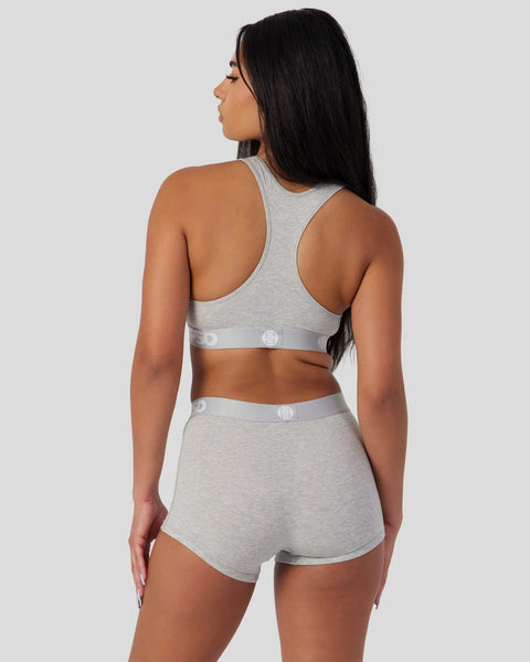 Woman wearing light grey racerback sports bra and matching shorts with button details, shown from back view.