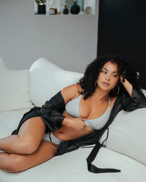 Woman wearing light grey athletic bra top, reclined on white couch.