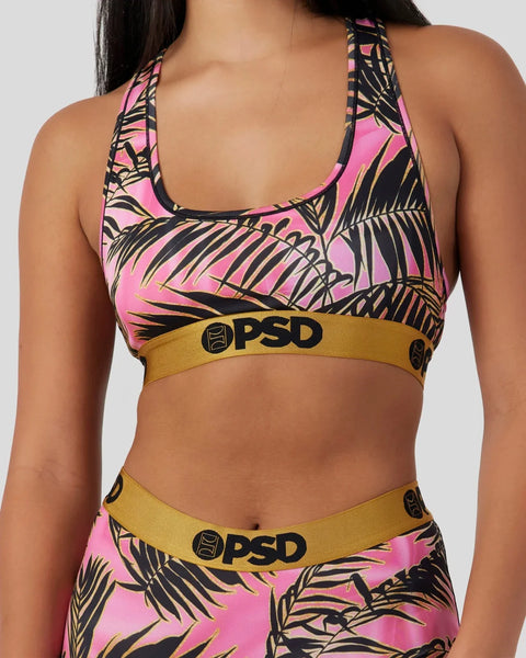 Pink sports bra with black and gold palm leaf print, gold waistband with PSD logo, matching bottoms visible.