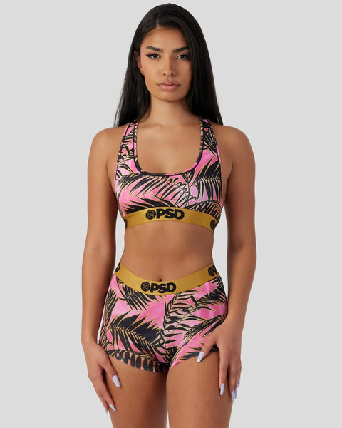 Woman wearing pink and black palm-print sports bra and matching shorts with gold OPSD waistbands.