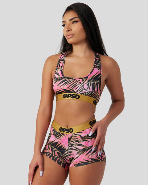 Woman wearing pink and black palm leaf print sports bra and shorts set with gold waistband.