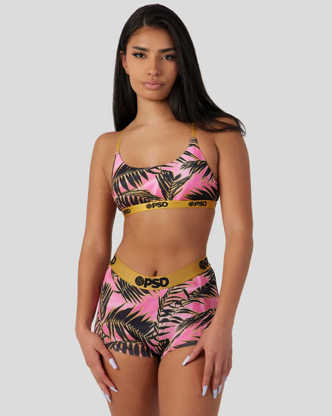 Woman wearing pink and black palm leaf patterned sports bra and matching shorts with yellow waistband trim.
