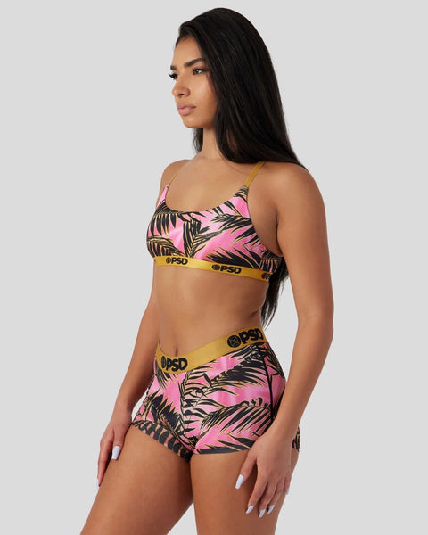 Woman wearing pink and black palm leaf patterned sports bra and shorts set with yellow branded waistbands.